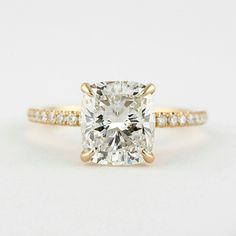 an engagement ring with a cushion cut diamond in the center and pave band around it