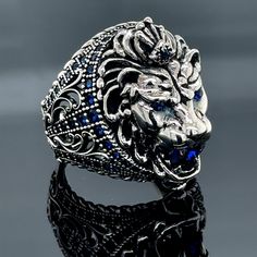 a lion head ring with blue stones in it's center on a reflective surface