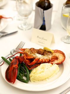 lobster, mashed potatoes and green beans are served on a white plate with silverware