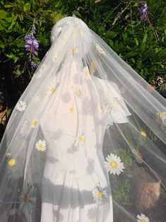 a veil with daisies on it sitting in front of some flowers