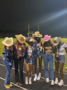 five girls in cowboy hats standing on the side of a road at night with their backs to the camera