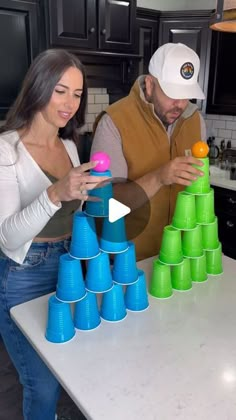 a man and woman standing in front of a stack of plastic cups on top of a kitchen counter