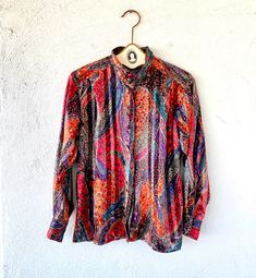 "Beautiful Warm Hues with Metallic gold threading throughout, this 1980s top has a very modern looking pattern. S p e c i f i c s . . . Label: Tess Tagged Size: 6 Approx Fit: XS - M depending on fit pref Color: Reds // Gold // Purple // Black // White // Blues Material: Silky Polyester // Buttons Condition: Overall in Amazing Vintage Condition M e a s u r e m e n t s . . . (side to side // laying flat // closed) Bust - approx. up to 21\" Waist - approx. up to 20\" Length - approx. 25\"" Colorful Patterned Shirt For Fall, Red Tops With Vibrant Print For Fall, Red Long Sleeve Blouse With Paisley Print, Red Vintage Shirt With Vintage Print, Red Vintage Print Shirt, Vintage Red Shirt With Floral Print, Vintage Multicolor Paisley Print Tops, Vintage Abstract Print Top For Fall, Vintage Red Shirt For Fall