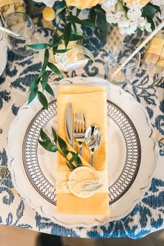 a place setting with yellow napkins, silverware and flowers on the tablecloth