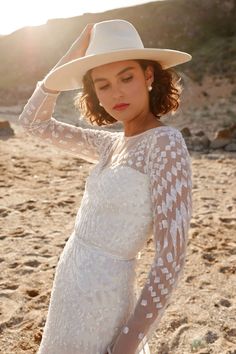 a woman in a white dress and hat on the beach