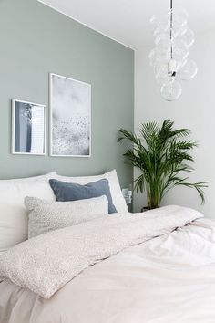 a bed with white sheets and pillows in a bedroom next to a potted plant