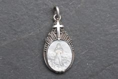 Art Deco pendant crafted from 835 silver, featuring a meticulously carved mother of pearl depiction of the Virgin Mary.  The pendant is adorned with elegant milgrain detailing and topped with a cross, the reverse is marked "835," attesting to its silver purity.  In very good condition, this piece is a stunning representation of both spiritual reverence and vintage craftsmanship, making it a perfect addition to any jewelry collection or a thoughtful gift for someone special. Measures 1.2cm x 2.1cm - whitout bail, weights 1.6 grams. Let me know if you would like further photos or information. Thanks for your visit! Classic White Medallion Jewelry, Silver Medallion With Mother Of Pearl, Silver Intaglio Round Pendant Necklace, Luxury Silver Necklace With Engraving Option, Silver Necklace With Intaglio Round Pendant, White Victorian Jewelry With Carved Details, White Miraculous Medal Pendant Jewelry, White Pendant Jewelry With Miraculous Medal, White Sterling Silver Jewelry With Engraving Option