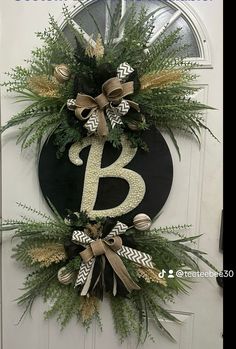 a wreath with the letter b on it hanging on a front door decorated with greenery