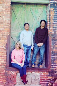 three people are posing for a photo in front of a wooden door with green shutters