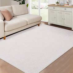 a living room with a white couch and rug on the wooden floor next to a window