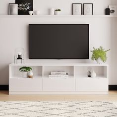 a flat screen tv sitting on top of a white entertainment center next to a potted plant