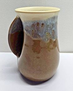 a brown and white vase sitting on top of a table next to a wall in the background