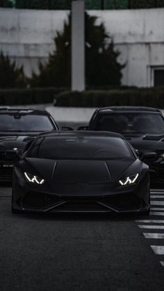 two black sports cars parked next to each other in a parking lot with lights on