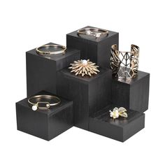 four black cubes with gold rings and bracelets on them, all stacked up