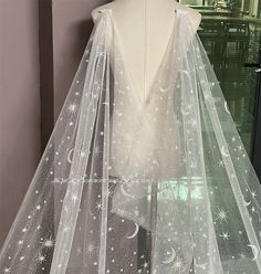 a white wedding veil with stars and moon designs on the front, sitting on a mannequin