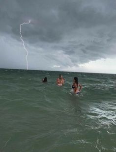 some people in the water and one is on a surfboard with a lightning behind them