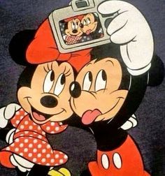 mickey and minnie mouse kissing in front of a camera on top of another cartoon character