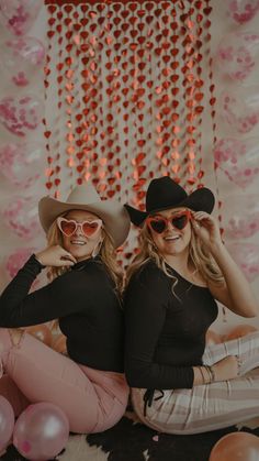 two women in cowboy hats and sunglasses posing for the camera with pink balloons behind them