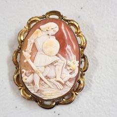 A very nice Victorian natural shell cameo brooch of St. George and the Dragon in a ornate rolled gold frame. The brooch is 2.5 x 2 .0 inch, the rolled gold part of the brooch is in fair to good condition with wear to the high points. The shell cameo is in excellent condition with no cracks or chips. The scene depicts the romantic version of the tale with St. George standing in full armour, minus the helm, and with a full head of hair, sword in hand and shield across his chest, straddling the Dra Ornate Carved Collectible Brooches, Ornate Carved Gold Brooches, Ornate Gold Carved Brooches, Ornate Cameo Brooch, Antique Cameo Brooch Collectible, Ornate Cameo Brooches For Collectors, Antique Cameo Brooches Collectible, Collectible Carved Gold Brooches, Antique Gold Cameo Brooch