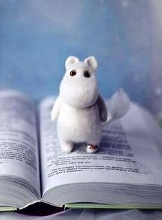 a white stuffed animal sitting on top of an open book with pages spread out to the side