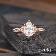 an engagement ring with a pear shaped diamond and two diamonds on the band, sitting on top of a rock