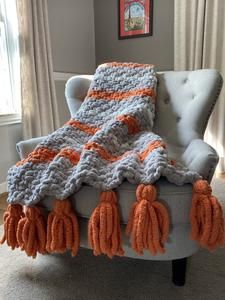 an orange and gray crocheted blanket sitting on top of a chair in front of a window