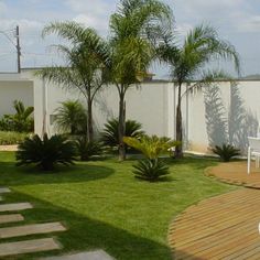 a garden with grass, trees and stepping stones on the ground in front of a white fence