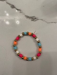 the multicolored beaded bracelet with gold beads is displayed on a marble surface