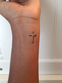 a small tattoo on the wrist of a person with a cross tattooed on their arm