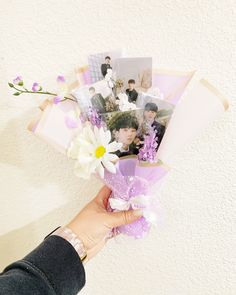 a person holding flowers and photos in their hand on a white wall with purple accents