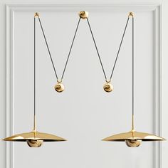 two gold pendants hanging from the ceiling in front of a white door with a black cord