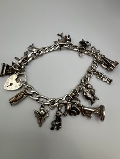 This beautiful vintage charm bracelet is made of sterling silver and contains 13 charms. The charms all reflect its mid-century character. Charms include a vintage phone, old fashioned car with moveable wheels, a baby with a crystal bead pacifier, and more. Bracelet is 7.75 inches in length and is closed with a heart lock charm connector. A truly special vintage piece.  As with all vintage Sterling silver, there can be some tarnishing. Many people enjoy this character and so I do not polish it--although it can be polished if you prefer. There is a bail attached without a charm but the 13 charms fill out the bracelet beautifully. Silver Vintage Charm Classic Jewelry, Vintage Antique Silver Sterling Bracelet, Vintage Nickel-free Sterling Silver Bracelet, Nickel-free Antique Silver Vintage Sterling Silver Bracelet, Collectible Classic Jewelry With Vintage Charm, Vintage Nickel-free Sterling Silver Bracelet In Antique Silver, Nickel Free Vintage Sterling Silver Bracelet, Nickel-free Vintage Sterling Silver Bracelet, Vintage Sterling Silver Bracelet In Antique Silver