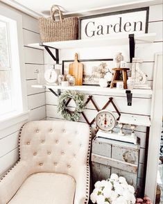 a white chair sitting in front of a window next to a shelf filled with flowers