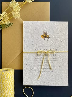 a yellow and white wedding card on top of a brown envelope next to a spool of twine