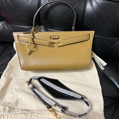 Tory Burch Lee Radziwill Cat Eye Bag Height: 5.3" (13.5cm); Length: 9.7" (24.5cm); Depth: 4.5" (11.5cm) High-end Tan Satchel For Daily Use, High-end Tan Bags For Office, High-end Tan Office Bags, High-end Tan Shoulder Bag With Branded Hardware, Designer Tan Satchel With Branded Hardware, Designer Tan Satchel For Office, High-end Tan Satchel With Top Carry Handle, Tan Satchel With Branded Hardware For Daily Use, Tan Top Handle Satchel With Branded Hardware