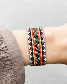 a woman's arm wearing an orange, black and white beaded bracelet