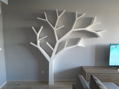 a living room with a tv and white tree sculpture on the wall in front of it