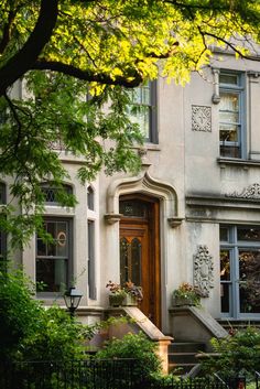 a large white building with a red door and window boxes on the front steps, surrounded by greenery