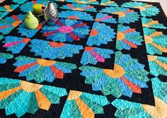 a quilted table topper with colorful flowers and vases sitting on the edge