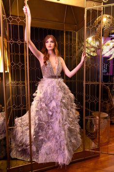 a woman in a purple dress is standing behind a golden gate and posing for the camera