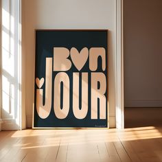 a framed poster with the words bonjou on it in front of a window and wooden floor