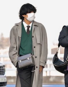 a man wearing a face mask while standing next to another man in a trench coat