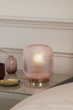 a pink glass table lamp sitting on top of a coffee table next to a vase