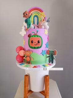 a birthday cake decorated with cartoon characters and balloons on a table in front of a gray background