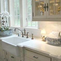 a white kitchen sink sitting under a window next to a counter with flowers on it