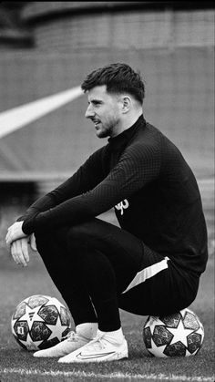 a black and white photo of a man sitting on the ground with two soccer balls