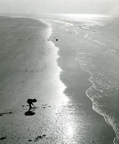 a black and white photo of a person walking on the beach near the water's edge