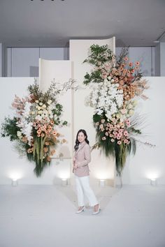 a woman standing in front of two tall floral arrangements with candles on either side of the wall