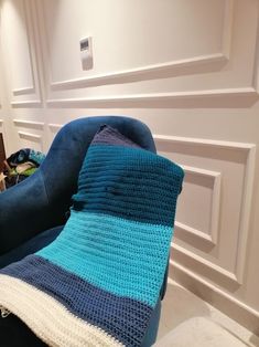 a blue chair with a crocheted blanket on it in front of a white wall