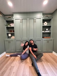 a man and woman sitting on the floor with their arms around each other in front of green cabinets